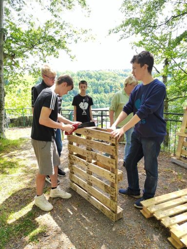 Gruppen von jungen Menschen bauen mit Holzpalette in einer natürlichen Umgebung.