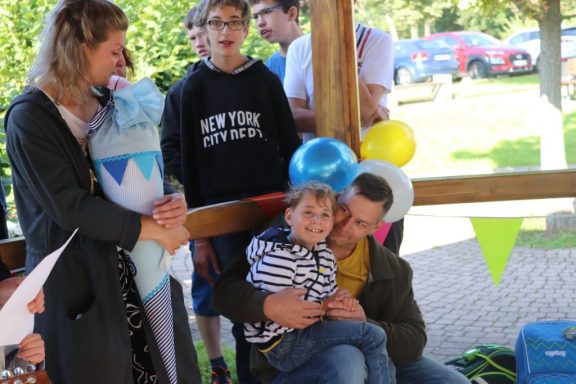 Ein Vater umarmt sein Kind, während andere Personen in der Nähe stehen und lächeln.