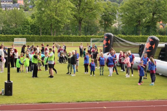 Gruppierung von Menschen auf einem Sportplatz, einige tragen farbige Westen.