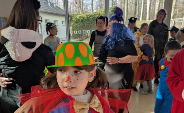 Kind mit lustigem Clownshut und roter Nase in einer festlichen Gruppenveranstaltung.