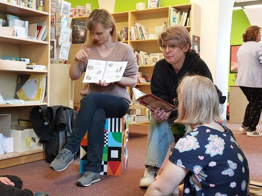 Zwei Frauen lesen Kindern in einer Bibliothek vor, während Kinder gebannt zuhören.