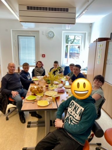 Gruppe von Personen sitzt an einem Tisch mit Essen und Getränken, lächelnde Atmosphäre.