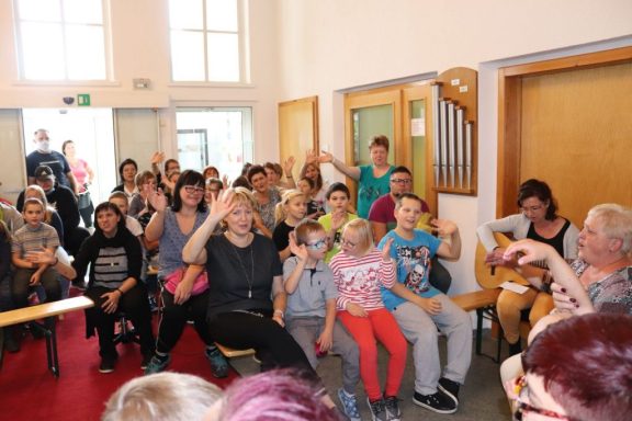 Eine Gruppe von Menschen sitzt in einem Raum und hebt die Hände.