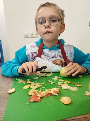 Ein Kind schält einen Apfel und sitzt an einem Tisch voller Obstschalen.