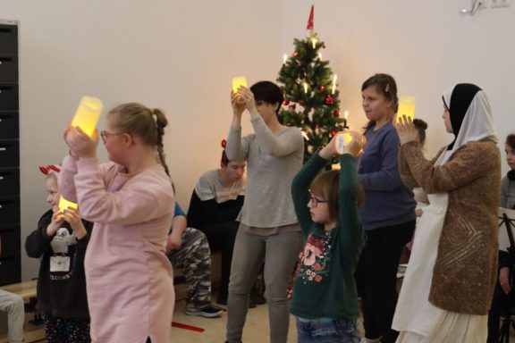 Gruppenevent mit Menschen, die leuchtende Laternen halten, vor einem Weihnachtsbaum.