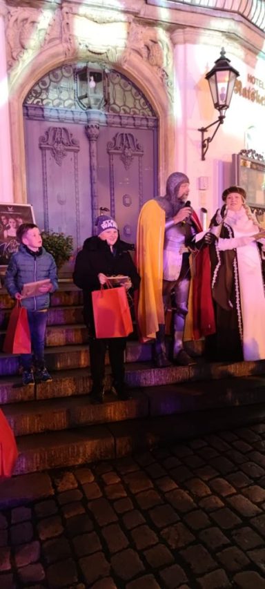 Menschen in historischen Kostümen stehen auf Stufen vor einem Gebäude mit Beleuchtung.