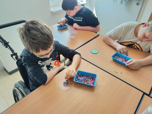 Drei Kinder arbeiten an einem Tisch mit bunten Bastelmaterialien.