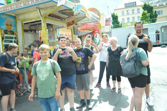 Gruppe von Menschen in einer lebhaften Umgebung, viele lächeln und halten Smartphones.
