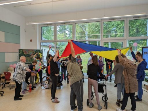 Gruppenspiel mit bunten Tüchern, Menschen stehen zusammen in einem Raum.