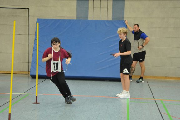 Junge mit Nummer 30 läuft durch Hindernisse, betreut von zwei Personen in Sportkleidung.