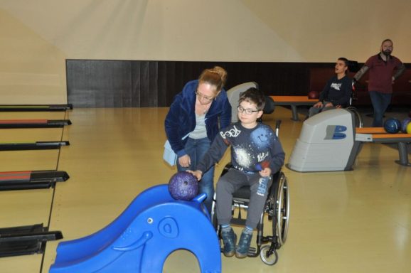 Ein Junge im Rollstuhl erhält Unterstützung beim Bowling von einer Frau.