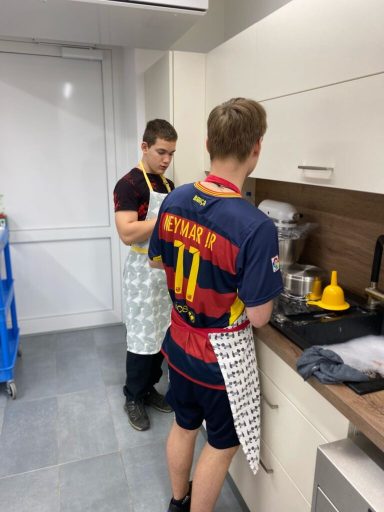 Zwei Jugendliche in Schürzen bereiten etwas in einer modernen Küche vor.