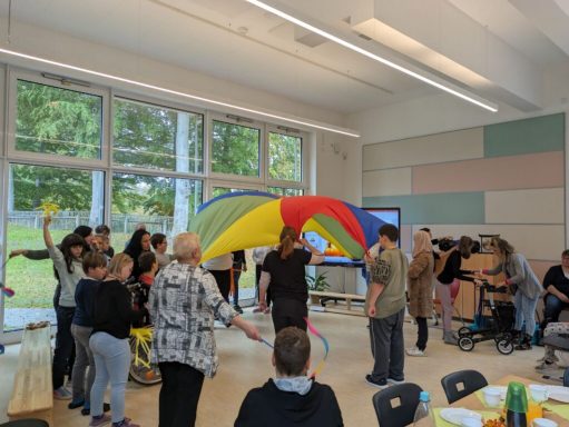 Gruppenspiel mit einem bunten Paragleitschirm in einem hellen Raum.