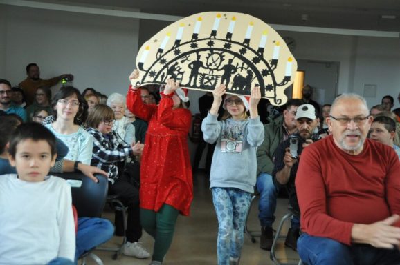 Kinder und Erwachsene im Publikum, zwei Kinder halten ein großes Schild hoch.