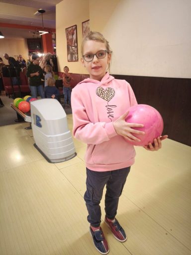 Mädchen in rosa Hoodie hält eine rosa Bowlingkugel in einer Bowlingbahn.