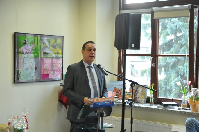 Mann in Anzug spricht am Mikrofon in einem hellen Raum mit Kunst an der Wand.