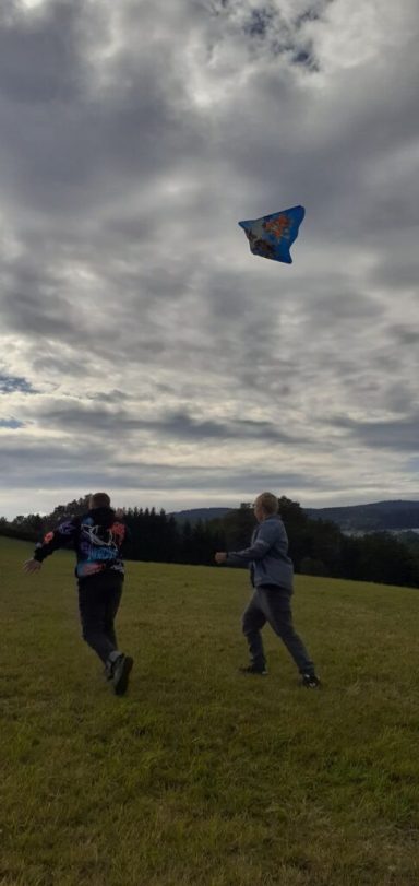 Zwei Menschen fliegen einen Drachen auf einer Wiese unter bewölktem Himmel.
