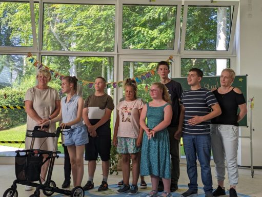 Gruppe von acht Personen steht in einem hellen Raum mit Fenster und Dekoration.