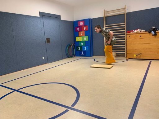 Junger Mann steht auf einer Plattform in einem Raum mit Sportgeräten und Farbkarten.