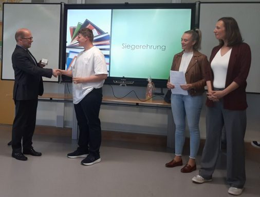 Zwei Personen schütteln sich die Hände, während andere Zuschauer anwesend sind.