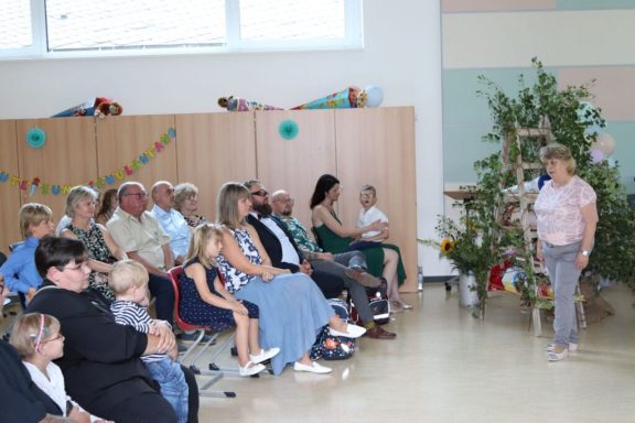 Feierliche Veranstaltung mit einer Menge von Erwachsenen und Kindern vor einem Weihnachtsbaum.