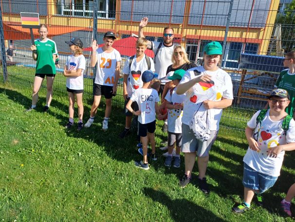 Gruppe von Kindern und Erwachsenen in T-Shirts mit Herzen, lächeln und winken.