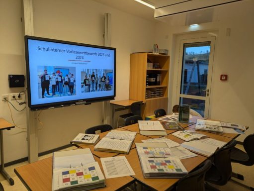 Besprechungsraum mit Präsentationsbildschirm und Materialien auf dem Tisch.