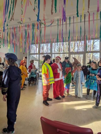 Menschen in Kostümen feiern in einem festlich dekorierten Raum mit bunten Bändern.