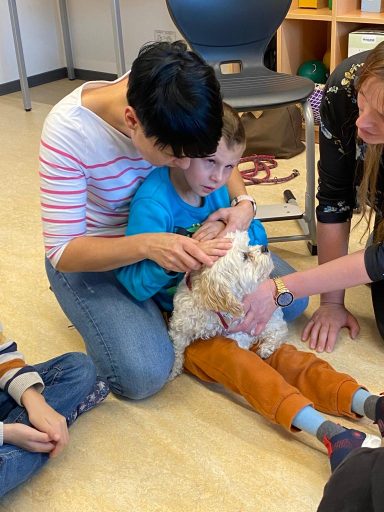 Ein Kind sitzt auf dem Boden und hält einen Hund, umgeben von Erwachsenen und anderen Kindern.