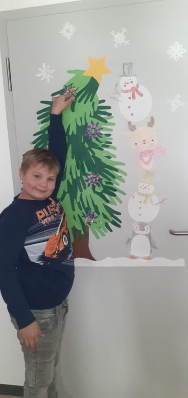 Ein Junge steht neben einem Weihnachtsbaum und Schneemännern an einer Wanddekoration.