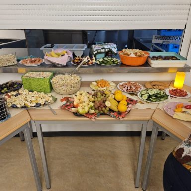 Bunt gefüllter Tisch mit verschiedenen Obst- und Gemüsesorten, Snacks und Salaten.