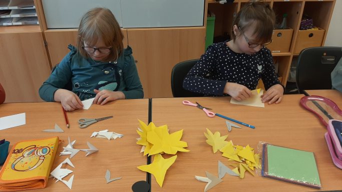 Zwei Mädchen basteln an einem Tisch mit Papier und Bastelmaterialien.