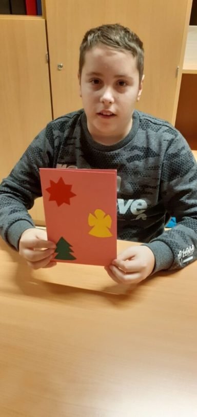 Ein Junge hält eine bastelnde Karte mit bunten Aufklebern in der Hand.