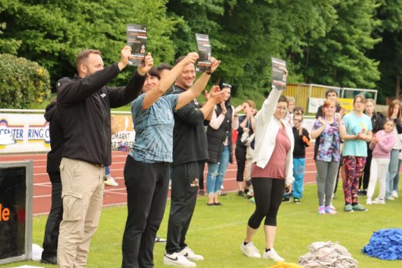 Personen bei einer Veranstaltung halten Bücher hoch, Menschen im Hintergrund applaudieren.