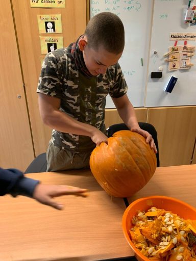 Junge schneidet einen Kürbis auf einem Tisch, daneben eine Schüssel mit Kürbiskernen.