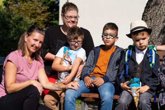 Eine Gruppe von vier Personen, darunter Kinder und Erwachsene, lächeln in der Sonne.