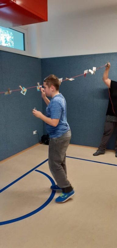 Junge in blauer Kleidung tanzt in einem Raum, während eine Person im Hintergrund steht.