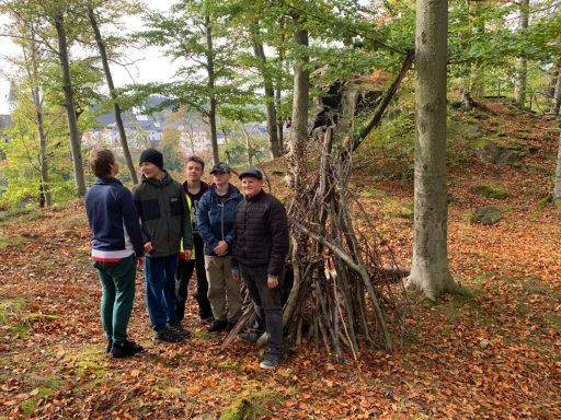 Fünf Personen stehen vor einer Baumstammstruktur im herbstlichen Wald.
