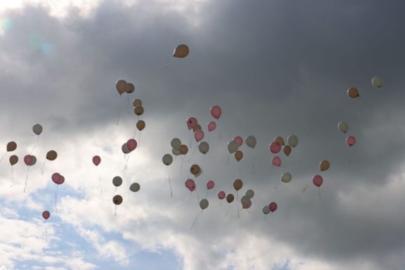 Bunte Luftballons schweben gegen einen bewölkten Himmel.