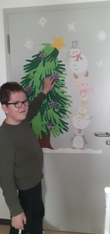 Ein Junge zeigt auf eine weihnachtliche Wanddekoration mit einem Baum und Schneemann.