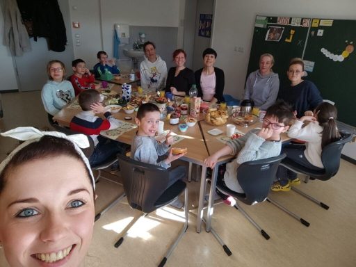 Eine Gruppe von Kindern und Erwachsenen sitzt um einen Tisch mit Snacks und Getränken.