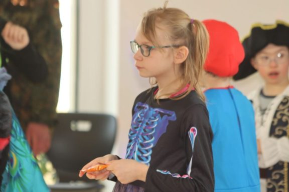 Mädchen mit Brille in bunter Verkleidung, beobachtet eine andere Szene.