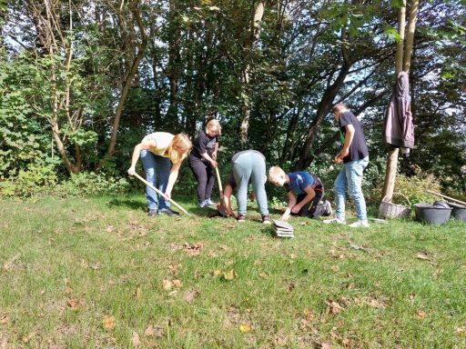 Sechs Personen arbeiten im Freien, graben in der Erde und pflanzen.