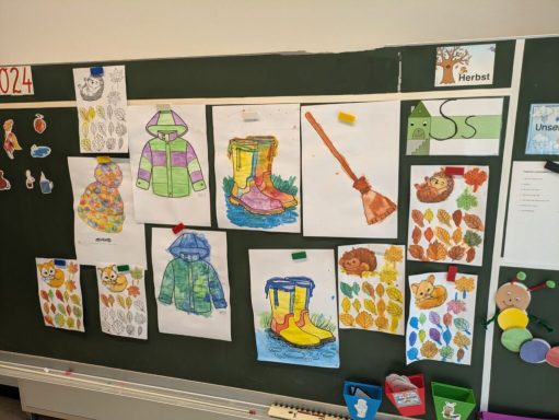 Bunte Zeichnungen von Gummistiefeln, Regenschirmen und Herbstblättern an einer Tafel.