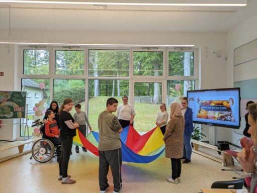 Menschen spielen mit einem großen bunten Fallschirm in einem hellen Raum.