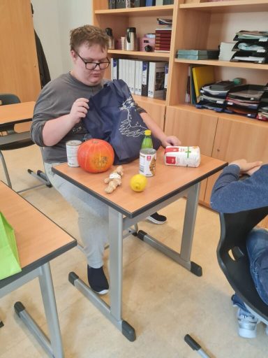 Junge mit Brille sitzt an einem Tisch, vor ihm liegen ein Kürbis, Getränke und Obst.