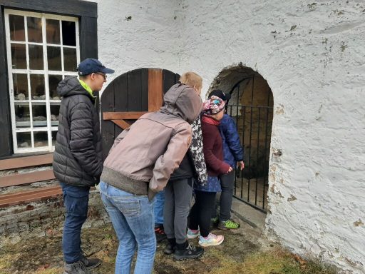 Gruppe von Personen schaut neugierig durch ein kleines Tor in einer Wand.