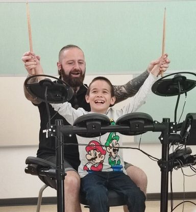 Ein lächelnder Mann und ein Kind spielen gemeinsam an einem Schlagzeug.