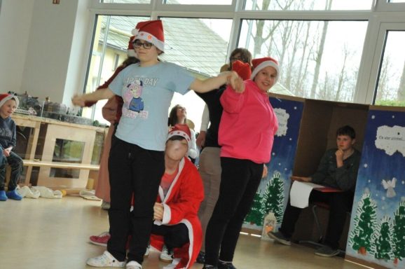 Gruppenaufführung mit Teilnehmern in Weihnachtsmann-Mützen und festlicher Kleidung.