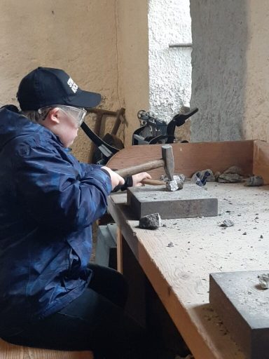 Eine Person arbeitet an einem Holzstück mit einem Werkzeug an einem Tisch.